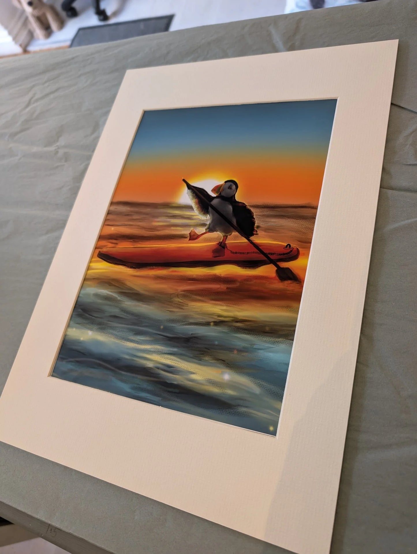 A sunset puffin illustration of a puffin paddleboaridng. A hand-painted puffin illustration, watercolour art of a puffin.
Painted on Anglesey by Welsh coastal/puffin artist Rachel Bennett